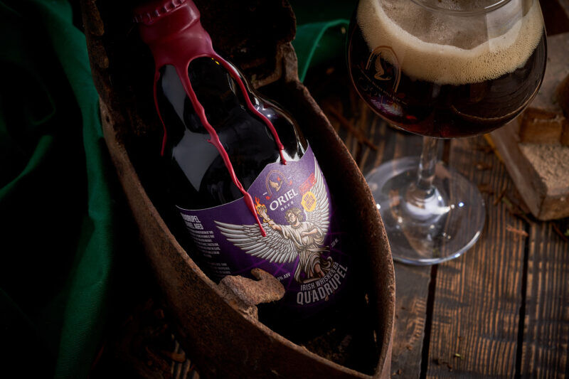 Belgian-style ale bottle with Oriel Beer branding and rustic background